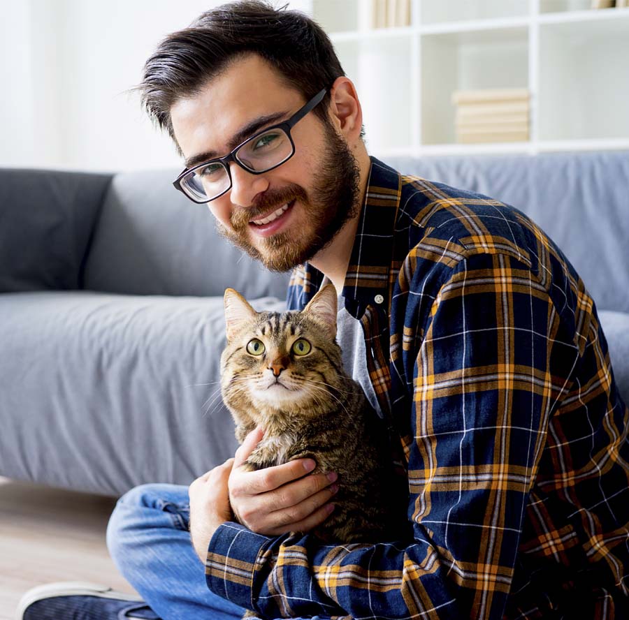 About Our Agency - Portrait of Smiling Man in Sitting in His Apartment Holding His Cat